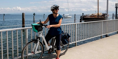 So sieht neuartige E+Bike Konzept von Lemmo One aus. Frau steht neben Ihrem E-Bike auf dem Steg von einem See.