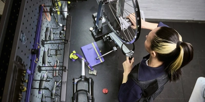 Eine Person repariert ein Fahrradrad an einem Arbeitstisch, umgeben von Werkzeugen.