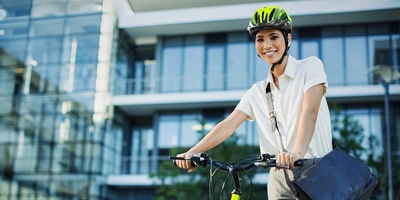 Lächelnde Frau in Businesskleidung mit Helm schiebt ihr Fahrrad vor einem Gebäude