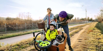 Du fährst. linexo regelt. Familie mit Fahrrad, Kind und Hund im Lastenrad auf einem Radweg im Freien