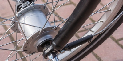 Nabendynamo reparieren – so wird’s gemacht Detailaufnahme eines Fahrradnaben mit Speichen und Gabel auf gepflastertem Boden.