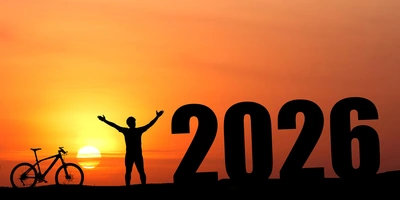Silhouette einer Person mit Fahrrad vor der untergehenden Sonne und der Zahl 2026.