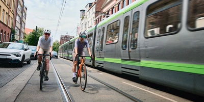 Zwei Radfahrer fahren entlang einer Straße, während eine Straßenbahn vorbeifährt.