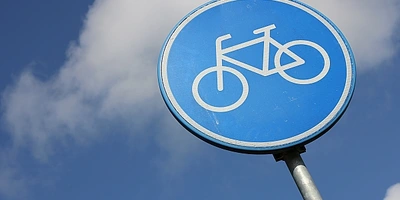 Blaue Fahrradsymbol-Schilder auf einem Pfosten vor einem Wolkenhimmel