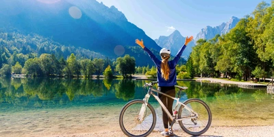 Frau steht mit Fahrrad neben klarem See im Sommer