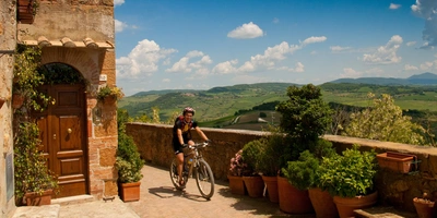 Überblick über die beliebtesten Radwege in Italien Fahrradfahrer auf einem gepflasterten Weg mit Blick auf eine grüne Landschaft.