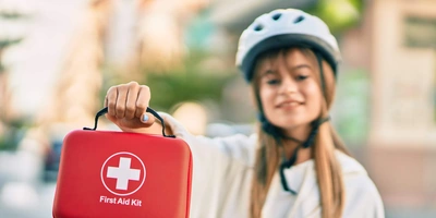 Frau hält eine Reiseapotheke in der Hand und trägt einen Fahrradhelm