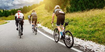 Radfahrer fahren auf einer Kurve in einer malerischen Landschaft mit Bäumen im Hintergrund.