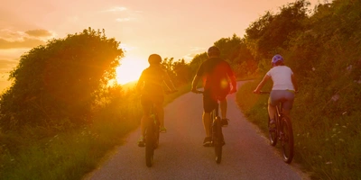 Drei Personen fahren mit E-Bikes im Sonnenuntergang