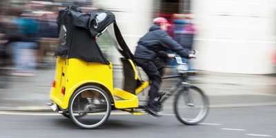 Radfahrer mit einem gelben Rikschawagen fährt an einer Menschenmenge vorbei