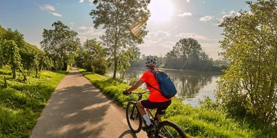 Frau fährt an einem Flussufer mit einem E-Bike entlang