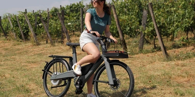 Frau sitzt auf E-Bike vor einem Weinfeld.
