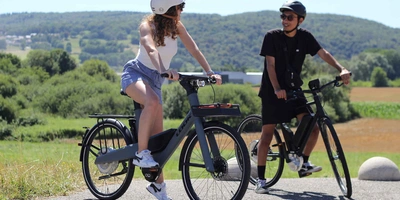 Mann und Frau mit Helm und Fahrrad vor grüner Landschaft.