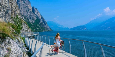 Frau mit Rad steht auf einer Brücke vor See in bergiger Landschaft