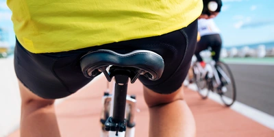Fokus auf den Fahrradfahrer mit gelbem Trikot, Blick auf den Sattel und Asphaltweg.
