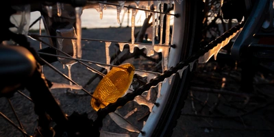 Detailaufnahme eines Fahrradkettenantriebs mit Eis und Sonnenlicht im Hintergrund.