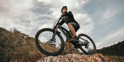 Mann steht mit Fahrrad auf einem Hang