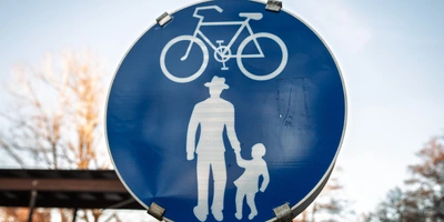 Blaues Straßenschild mit einem weißen Fahrrad und einem Erwachsenem mit Kind