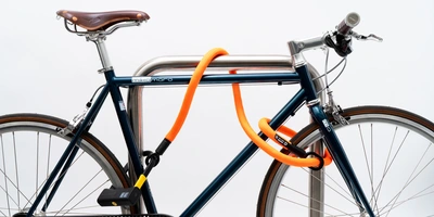 Blaues Fahrrad mit einem orangefarbenen Schloss, an einem Metallpfosten gesichert.