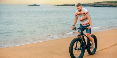Mann fährt auf Fatbike Strand entlang.