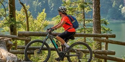 Frau mit Helm fährt auf E-Mountainbike durch Wald.