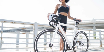 Frau steht neben Rennrad vor Geländer von Brücke.