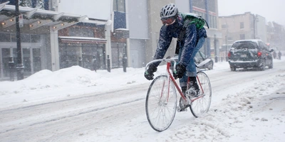Winterbekleidung fürs Fahrradfahren Radfahrer kämpft bei starkem Schneefall auf einer verschneiten Straße.