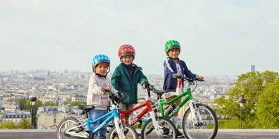 Woom Kinderfahrräder in unterschiedlichen Farben und Größen Drei Kinder auf Fahrrädern mit Helmen