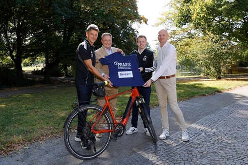 Vier Personen stehen im Freien und halten ein T-Shirt vor einem Fahrrad.