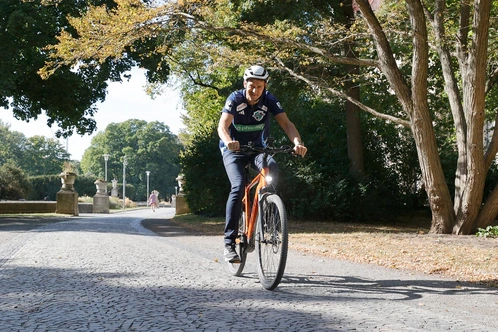 Christian Prokop fährt lächelnd auf einem Kiesweg in einem Park.