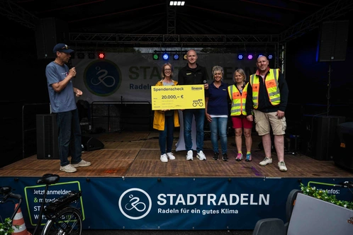 Gruppenevent mit Personen auf einer Bühne, die einen großen Scheck präsentieren.