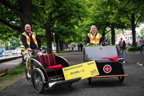 Zwei Personen in leuchtenden Westen stehen neben einem Fahrrad-Rickshaw in einem Park.