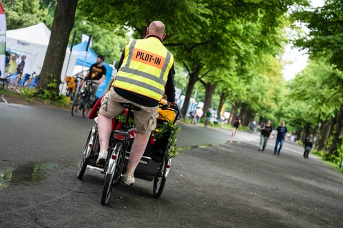 Eine Person im Warnwesten fährt mit einem Fahrradanhänger auf einem gepflasterten Weg.