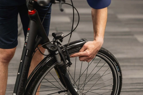 Ein Mann überprüft das Vorderrad eines schwarzen E-Bikes in einem modernen Raum.