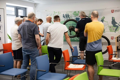 Eine Gruppe von Männern schaut an einer Wand eine Fahrradausstellung an.
