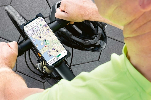 Nahaufnahme von Händen, die einen Fahrradlenker halten, während ein Smartphone eine Karte zeigt.