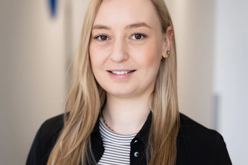 Junge Frau mit blonden Haaren, lächelnd, in einem modernen Büro.