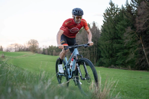 Ein Mountainbiker fährt einen hügeligen Feldweg, umgeben von Bäumen.