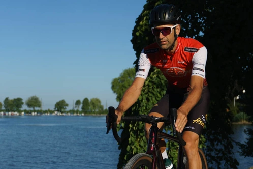 Radfahrer in einem roten Trikot fährt am Ufer eines Gewässers entlang.